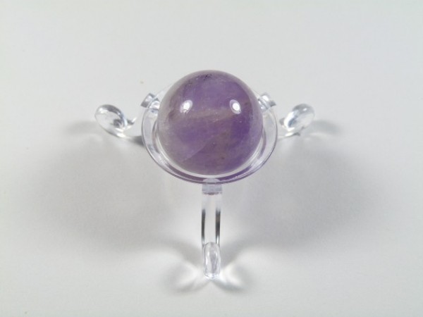 Kula ametyst szlifowany średnica 2,5 cm. Fioletowa kulka ametystu na przezroczystej podstawce, na białym tle.
