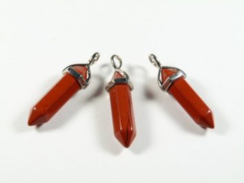 Trzy czerwone kamienie w formie wisiorów z metalowymi okuciami na białym tle.