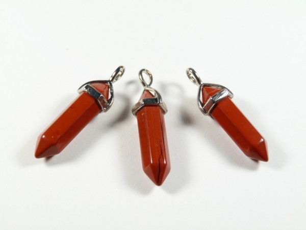 Trzy czerwone kamienie w formie wisiorów z metalowymi okuciami na białym tle.