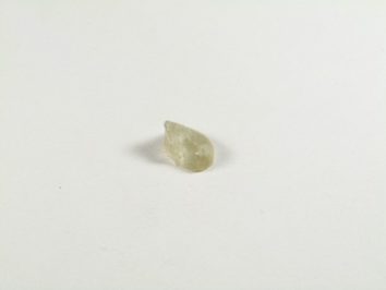 Prasiolit/ prazjolit - kamień gładzony, polerowany. Mały, jasnozielony kamień leży na białym tle.