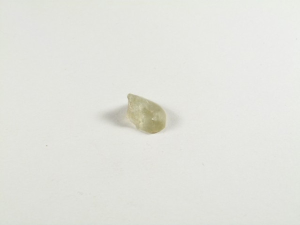 Prasiolit/ prazjolit - kamień gładzony, polerowany. Mały, jasnozielony kamień leży na białym tle.