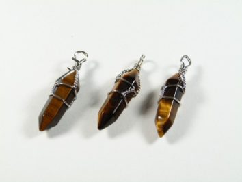 Trzy wiszące wisiorki z kamieni tygrysiego oka oplecione srebrnym drutem na białym tle.