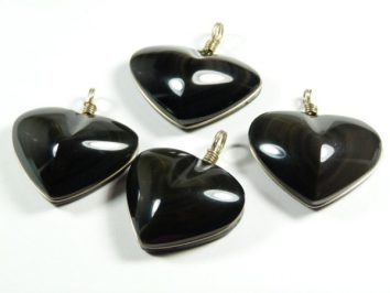 Cztery czarne, błyszczące wisiorki w kształcie serca leżą na białym tle.