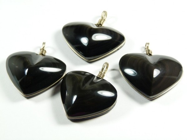 Cztery czarne, błyszczące wisiorki w kształcie serca leżą na białym tle.