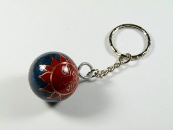 Breloczek z metalowym kółkiem i kulką ozdobioną czerwonym słońcem na niebieskim tle.