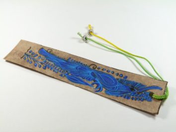 Ręcznie wykonana zakładka do książki z niebieskim rysunkiem ptaka i kolorowymi sznurkami.