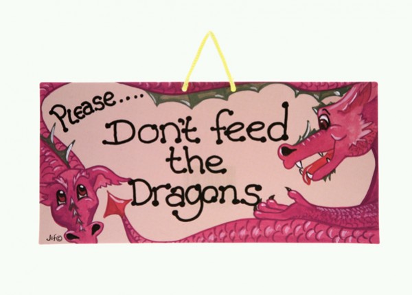 Różowa tabliczka z napisem "Please... Don't feed the Dragons" i rysunkiem dwóch smoków.