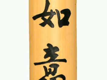 Drewniany zwój z chińskimi znakami kaligraficznymi, zawieszony na czerwonym sznurku.