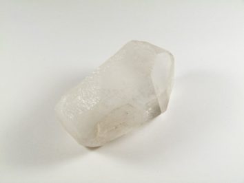 Przezroczysty kryształ kwarcu leży na białym tle.