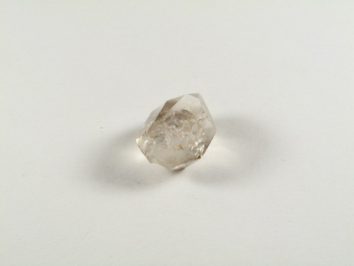 Kwarc dymny - kamień naturalny, surowy, nieszlifowany. Przezroczysty kryształ kwarcu leży na białym tle.