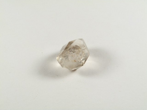 Kwarc dymny - kamień naturalny, surowy, nieszlifowany. Przezroczysty kryształ kwarcu leży na białym tle.