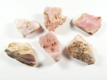 Sześć kawałków różowego kamienia mineralnego na białym tle.