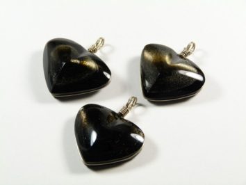 Trzy czarne, błyszczące zawieszki w kształcie serca na białym tle.
