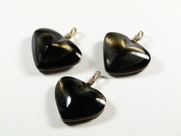 Trzy czarne, błyszczące zawieszki w kształcie serca na białym tle.