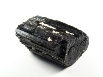 Czarny turmalin - kamień naturalny, surowy, nieszlifowany. Czarny, błyszczący kryształ turmalinu na białym tle.
