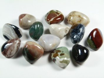 Sardoniks/ sardonyks - kamień gładzony, polerowany, szlifowany i bębnowany w formie otoczaka. Kilka kolorowych, wypolerowanych kamieni ozdobnych leży na białym tle.