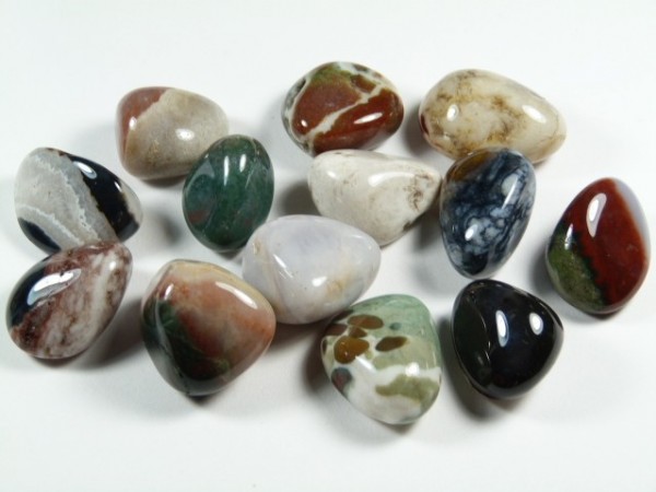 Sardoniks/ sardonyks - kamień gładzony, polerowany, szlifowany i bębnowany w formie otoczaka. Kilka kolorowych, wypolerowanych kamieni ozdobnych leży na białym tle.