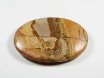Jaspis obrazkowy - kamień gładzony, polerowany, szlifowany. Gładki, owalny kamień jaspis o brązowych i beżowych smugach leży na białym tle.
