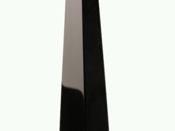 Czarny obelisk z gładkimi ścianami, stojący pionowo na jasnym tle.