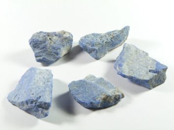 Pięć nieoszlifowanych, niebieskawych kawałków minerału leży na białym tle.