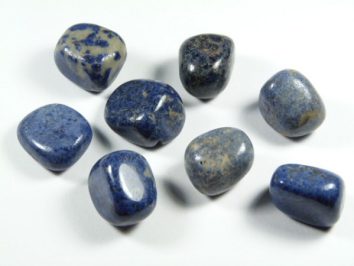 Dumortieryt - kamień gładzony, polerowany, szlifowany i bębnowany w formie otoczaka. Osiem niebieskich, wypolerowanych kamieni leży na białym tle.