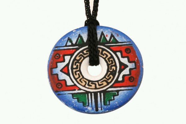 Okrągły, kolorowy wisiorek z motywem azteckim zawieszony na czarnym sznurku.