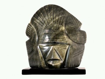 Kamienna rzeźba stylizowanej głowy na ciemnej podstawie, ukazana z przodu.