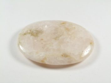 Kalcyt - kamień gładzony, polerowany, szlifowany. Wypolerowany, różowy kamień kalcytu leży na białym tle.