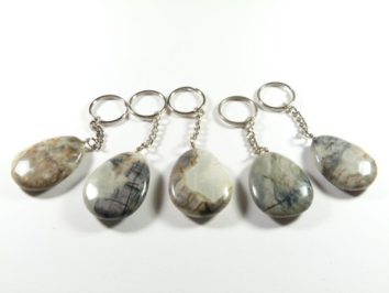 Pięć breloków z owalnymi kamieniami na srebrnych łańcuszkach leży na białym tle.