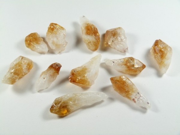 Kilka surowych kryształów cytrynu o żółto-brązowym zabarwieniu leży na białym tle.