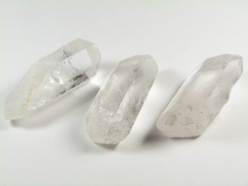 Trzy przezroczyste kryształy kwarcu leżące na białym tle.