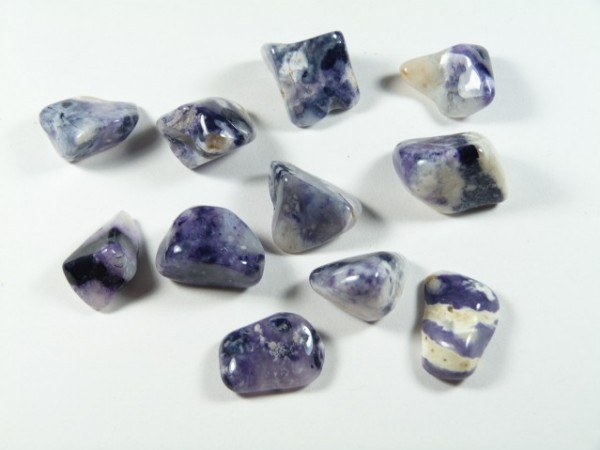 Polerowane kamienie o fioletowych i białych odcieniach leżące na białym tle.