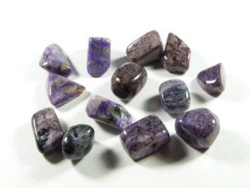 Fioletowe, wypolerowane kamienie leżące na białym tle.