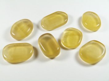 Siedem żółtych, gładkich kamieni leży na białym tle.