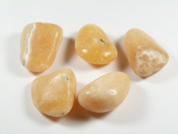 Kalcyt złoty - kamień gładzony, polerowany, szlifowany i bębnowany w formie otoczaka. Pięć gładkich, polerowanych, żółtych kamieni leży na białym tle.