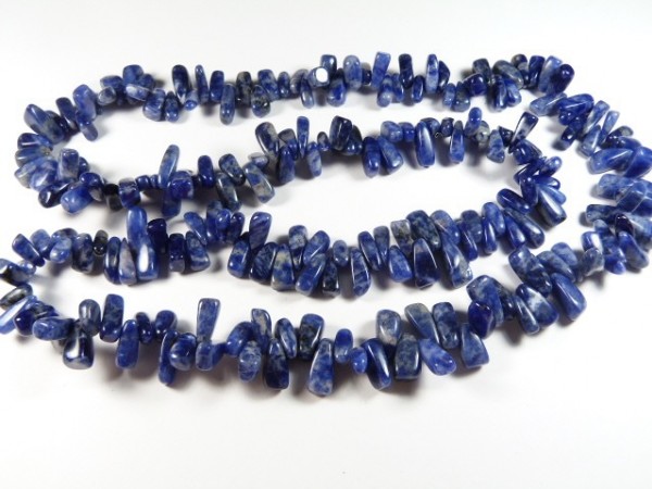 Naszyjnik z nieregularnych, niebieskich kamieni ułożonych na białym tle.