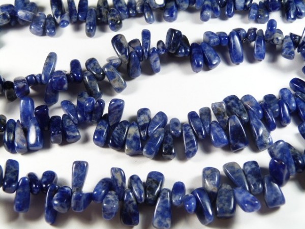 Nawleczone na sznurek niebieskie kamienie ozdobne leżące na białym tle.