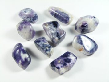 Dziewięć polerowanych kamieni o fioletowo-białym zabarwieniu na białym tle.