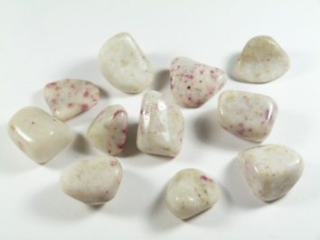 Gładkie białe kamienie z drobnymi różowymi plamkami, ułożone na białym tle.