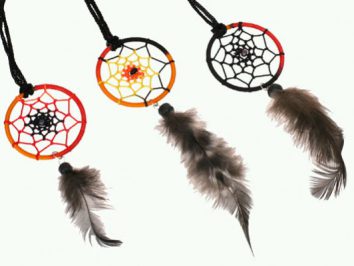 Trzy kolorowe łapacze snów z piórami wiszą na czarnych sznurkach.