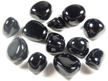 Onyks czarny - kamień gładzony, polerowany, szlifowany i bębnowany w formie otoczaka. Kilka wypolerowanych, czarnych kamieni ułożonych na białym tle.