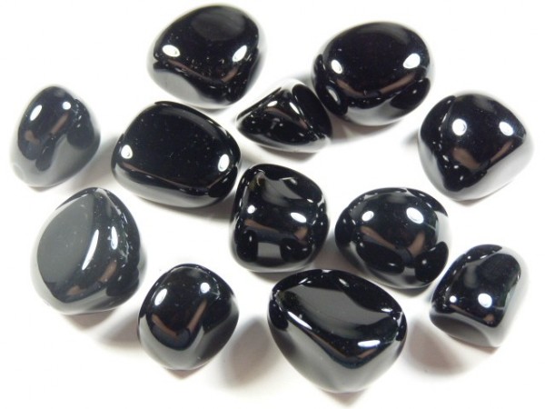 Onyks czarny - kamień gładzony, polerowany, szlifowany i bębnowany w formie otoczaka. Kilka wypolerowanych, czarnych kamieni ułożonych na białym tle.