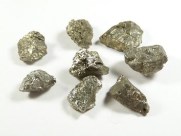 Piryt - kamień naturalny, surowy, nieszlifowany. Siedem kawałków srebrzystego metalu na białym tle.