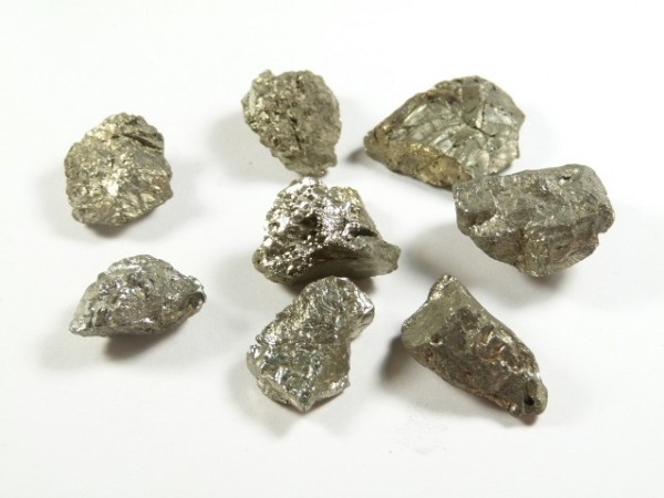 Piryt - kamień naturalny, surowy, nieszlifowany. Siedem kawałków srebrzystego metalu na białym tle.