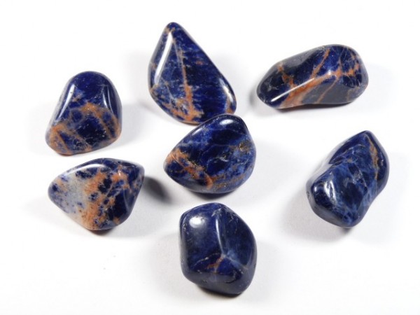 Siedem wypolerowanych, niebieskich kamieni z jasnymi żyłkami leży na białym tle.