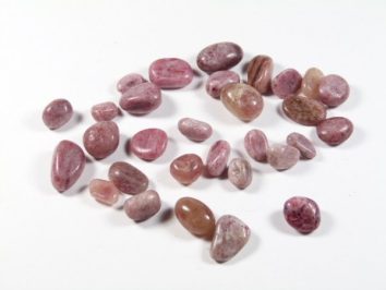 Kilka gładkich, różowych kamieni leży rozrzuconych na białym tle.