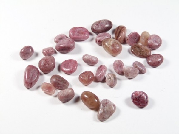 Kilka gładkich, różowych kamieni leży rozrzuconych na białym tle.