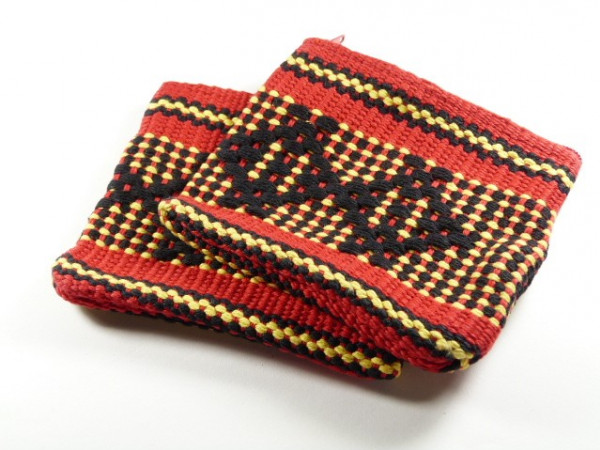 Dwie kolorowe, tkane rękawice kuchenne z czerwonym, czarnym i żółtym wzorem ludowym.