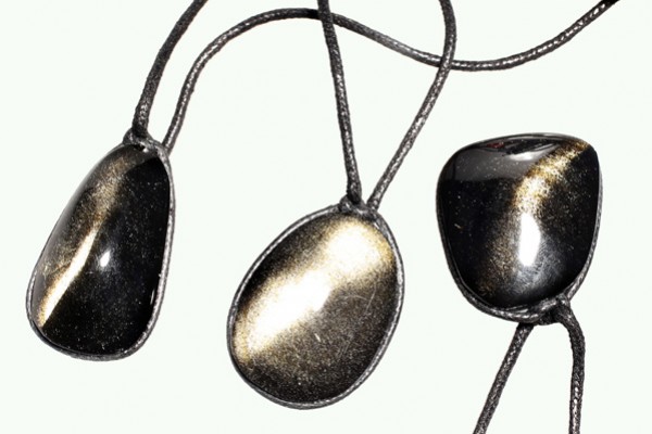 Trzy czarne obsydianowe wisiorki na czarnych sznurkach, ułożone obok siebie.