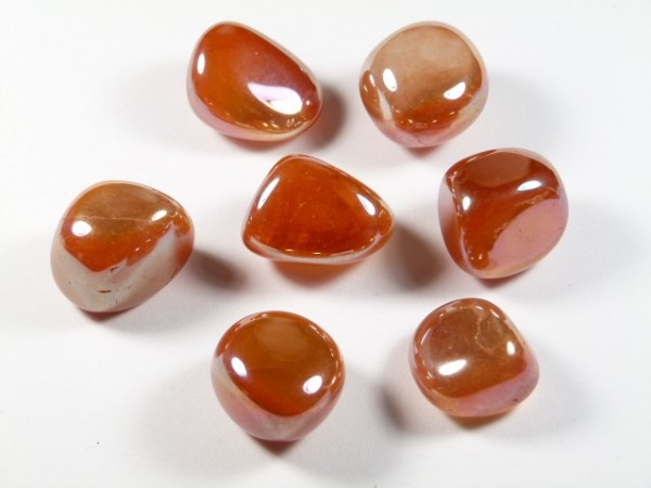 Siedem gładkich, polerowanych kamieni w odcieniach pomarańczowo-brązowych na białym tle.